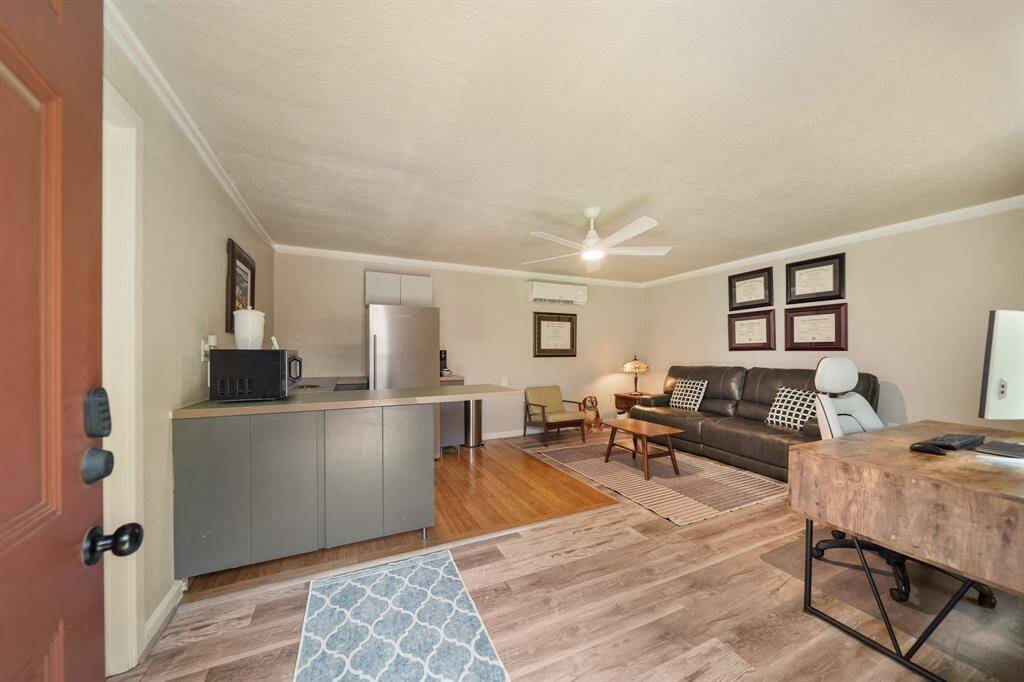 This guest house showcases a cozy living space with an open layout. It features a small kitchenette with modern appliances. The room has a mix of wood and laminate flooring, natural light and a ceiling fan enhance the ambiance.