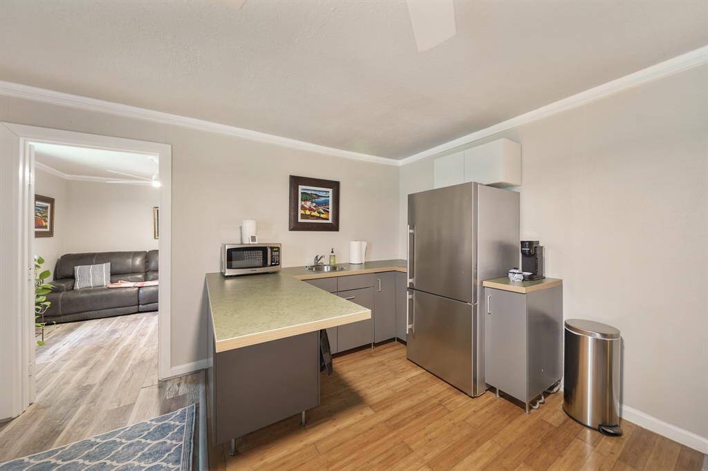 This photo shows a modern kitchenette with stainless steel appliances, including a fridge and microwave. The countertops are spacious, and a doorway leads to a cozy bedroom.