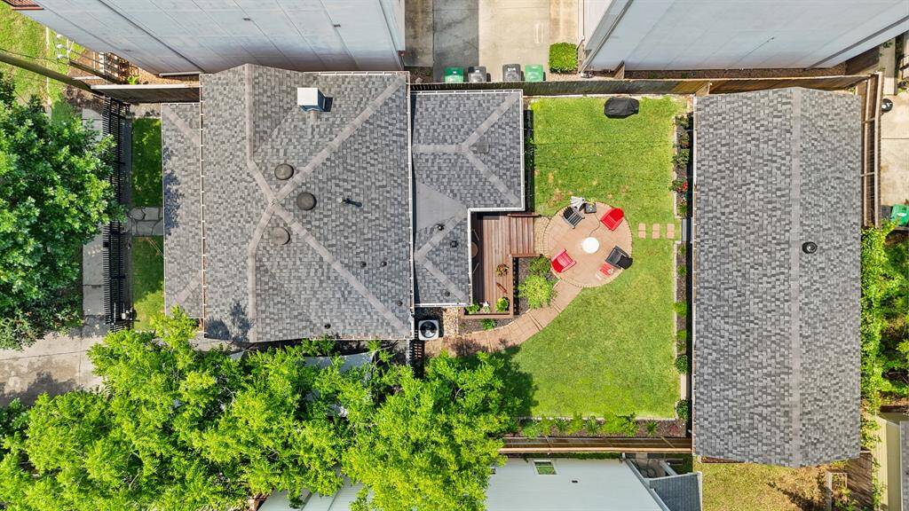 This aerial view shows a home with a spacious backyard featuring a circular patio with seating, and a pathway leading to the house. The property is framed by greenery, offering privacy and a cozy outdoor space.