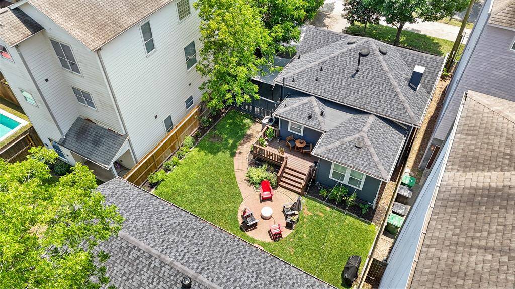 This aerial view shows a home with a spacious backyard featuring a circular patio with seating, and a pathway leading to the house. The property is framed by greenery, offering privacy and a cozy outdoor space.