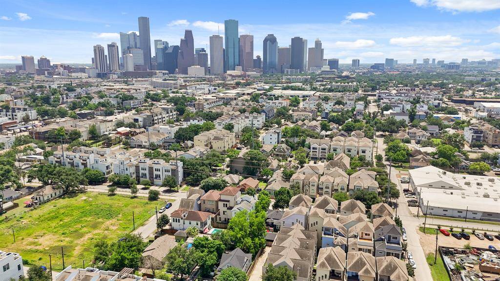 This aerial photo showcases a vibrant urban neighborhood with a mix of modern townhouses and greenery, set against a backdrop of a prominent city skyline. Ideal for those seeking urban living with proximity to city amenities.