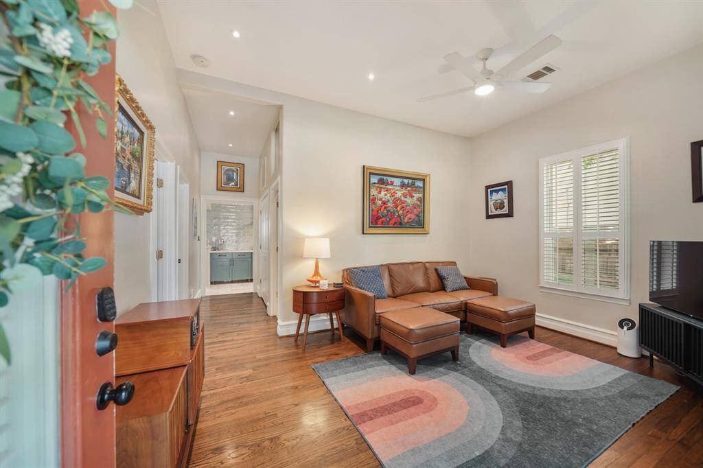 This cozy living area features hardwood floors with natural light flowing through plantation shutters, and the hallway leads to a stylish kitchen.