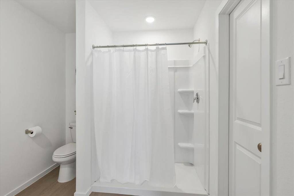 The spacious primary bathroom features an enlarged shower, elegant vinyl plank flooring, and a crisp all-white color scheme, enhancing the clean and airy feel of the space.