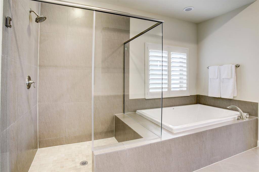 Spacious walk-in shower with glass doors and a large built-in bathtub. The neutral-toned tiles and modern fixtures create a sleek, contemporary look.