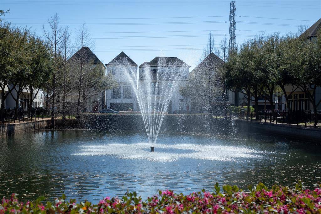 A serene residential area with a pond featuring a central fountain. Includes charming houses and tree-lined pathways, creating a tranquil and picturesque setting.
