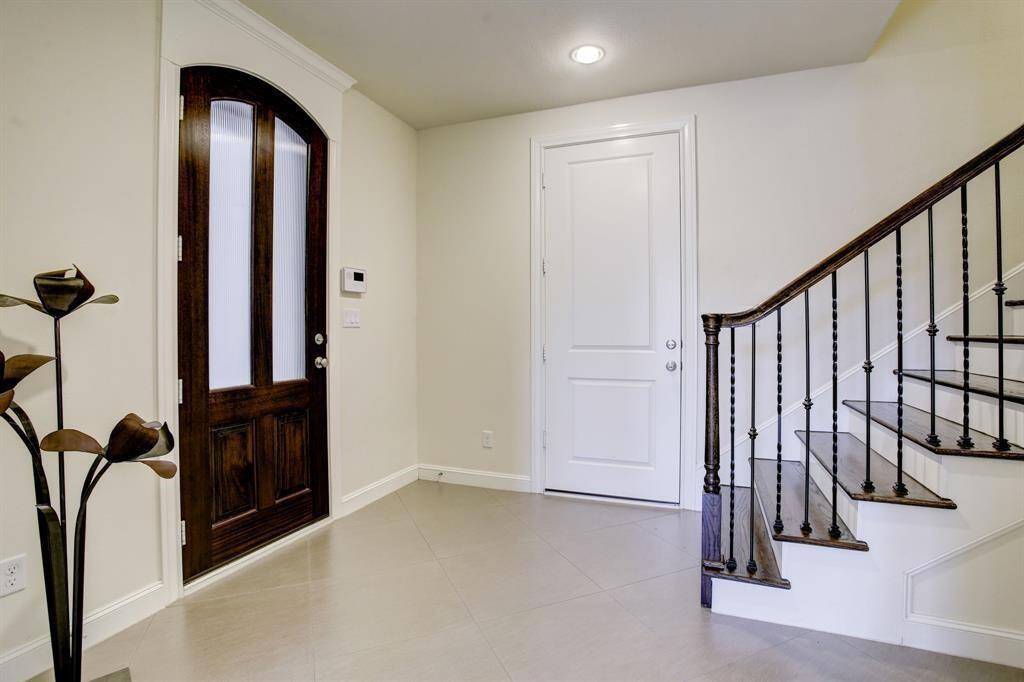 Bright entryway featuring a dark wooden front door with frosted glass panels, a sleek staircase with wrought iron railings, and neutral tile flooring.