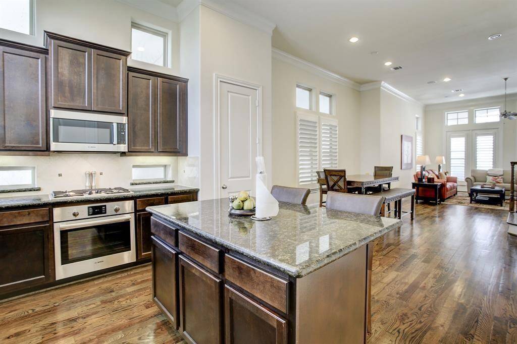 An open-concept kitchen and living area with wood cabinetry, granite countertops, and hardwood floors.