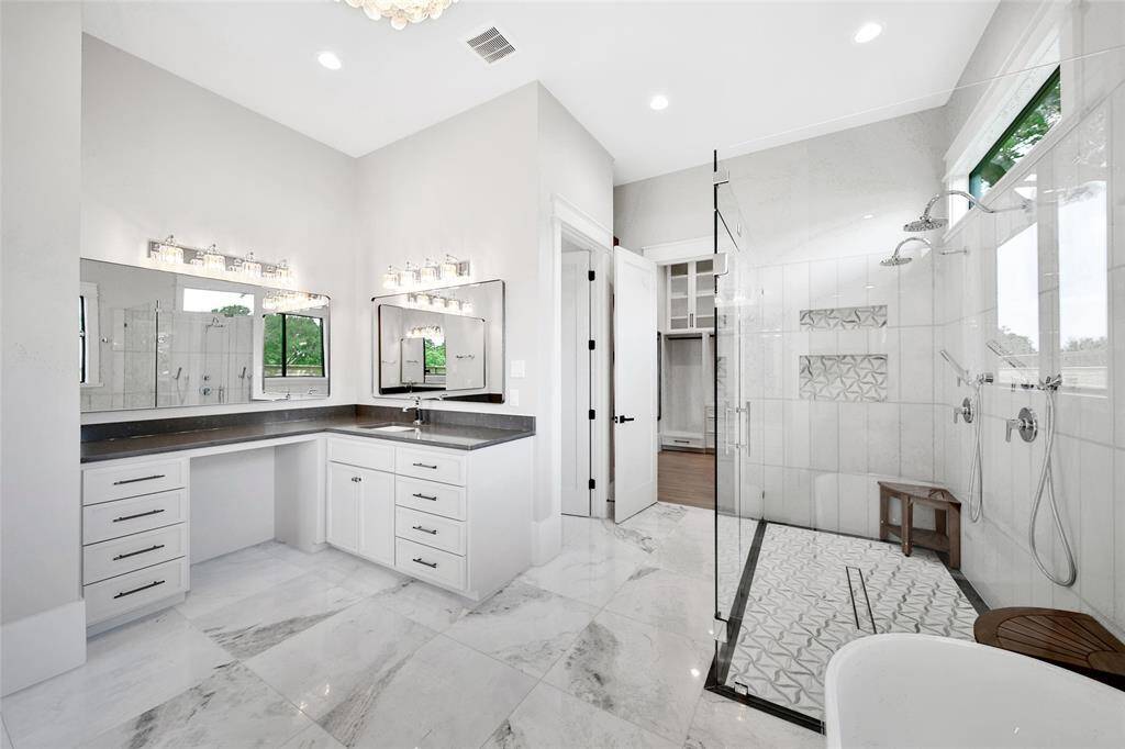 Beautiful stone countertops is paired with natural stone flooring, while the frameless glass shower helps to showcase custom tile work and finishes.