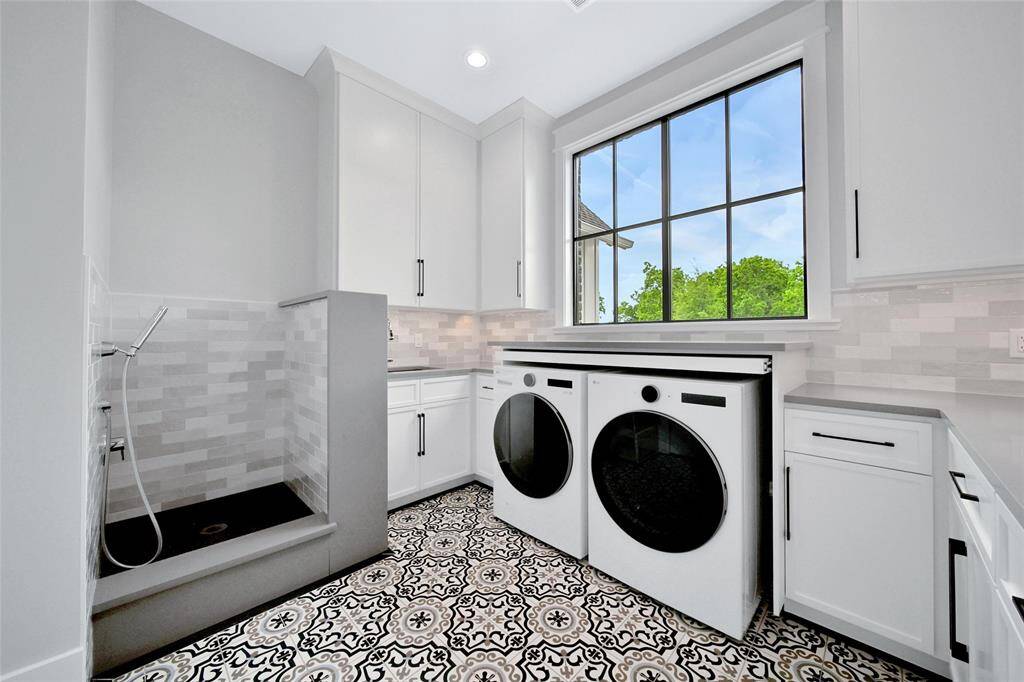 Laundry with Pet Washing Station, encased washer and dryer with pullout additional shelving for folding and plenty of cabinets and drawers for more storage.
