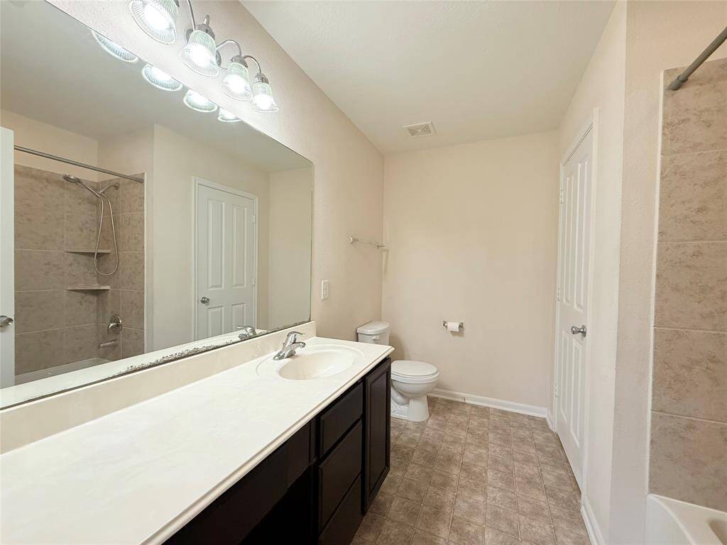 This photo shows a compact laundry room featuring a washer and dryer, a small window for natural light, and a shelf for storage. The room has a neutral color scheme and tile flooring.