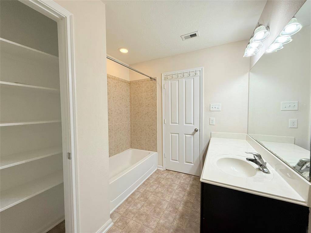 This bathroom features a sleek design with a large mirror, single sink vanity, and tiled shower area. The space is well-lit with modern fixtures, and it includes a toilet and ample counter space.