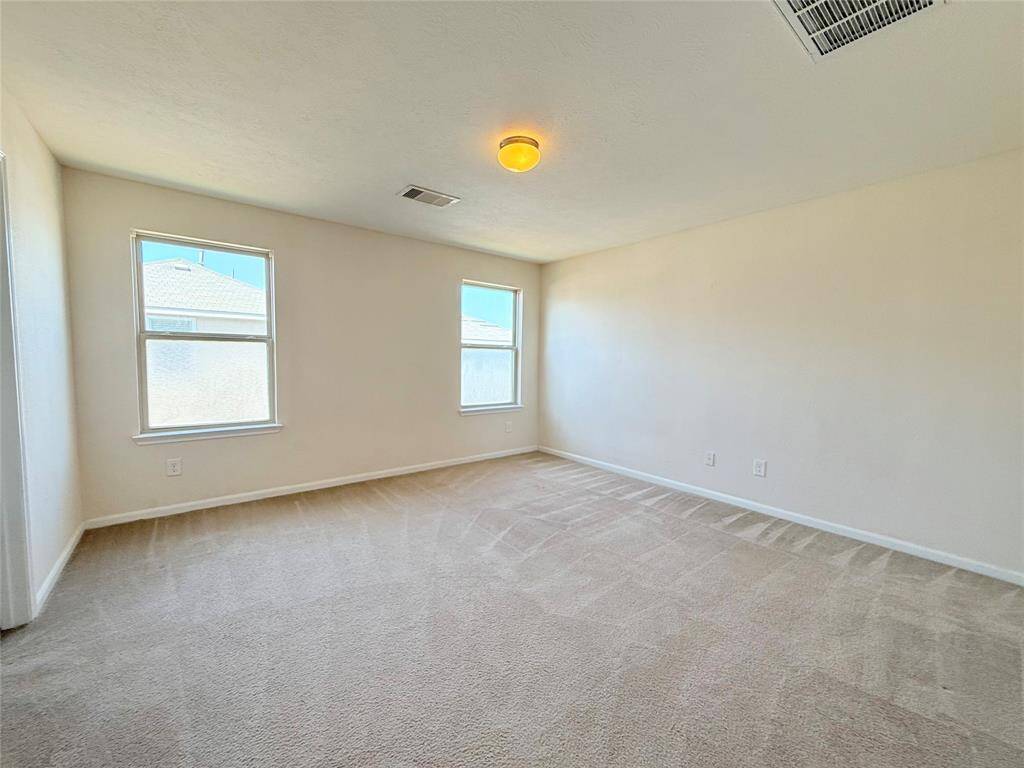 This is a cozy bedroom with neutral-colored walls and carpet, featuring a window with blinds allowing natural light, a ceiling light fixture, and a small closet with a sliding door.