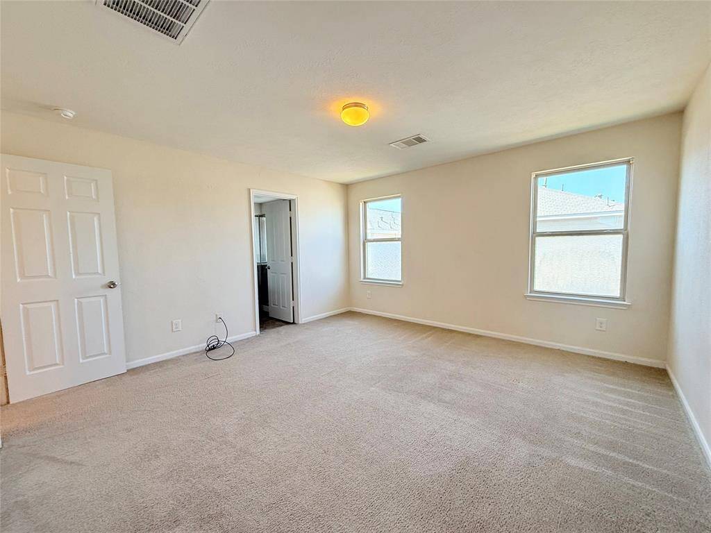 This spacious, carpeted bedroom features neutral walls, two large windows providing ample natural light, and a ceiling light fixture.