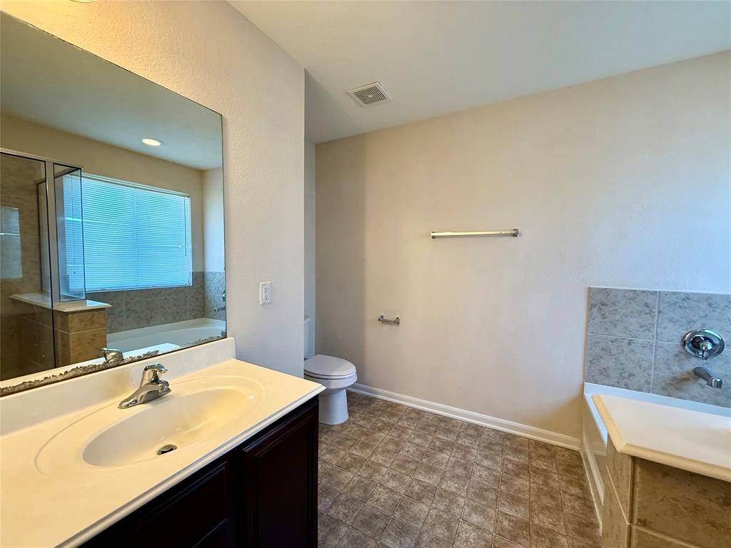 Bright bathroom featuring a large bathtub, separate glass-enclosed shower, single vanity, and ample natural light through a window with blinds.