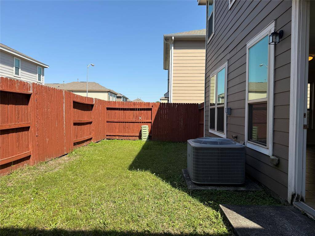 Cozy backyard with a grassy area, bordered by a wooden fence. The space features an external air conditioning unit and is accessible from the house, offering potential for outdoor relaxation or gardening.