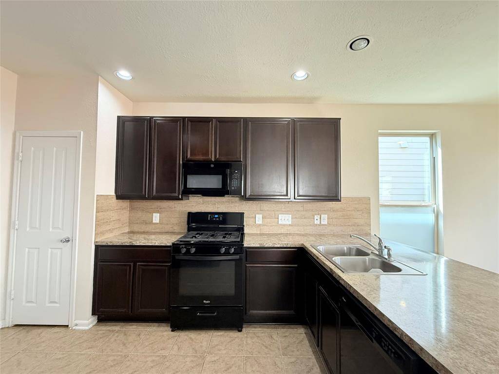Modern kitchen with dark wood cabinets, granite countertops, and tiled backsplash. Features a gas stove, built-in microwave, and double sink. Bright and spacious with recessed lighting.