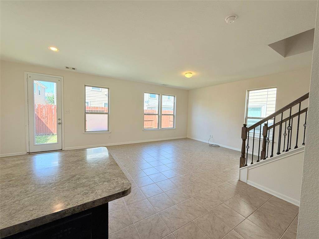 Bright, open living area with large windows and tile flooring. Features a staircase with decorative railings and a door leading to the backyard. Ideal for entertaining and family gatherings.