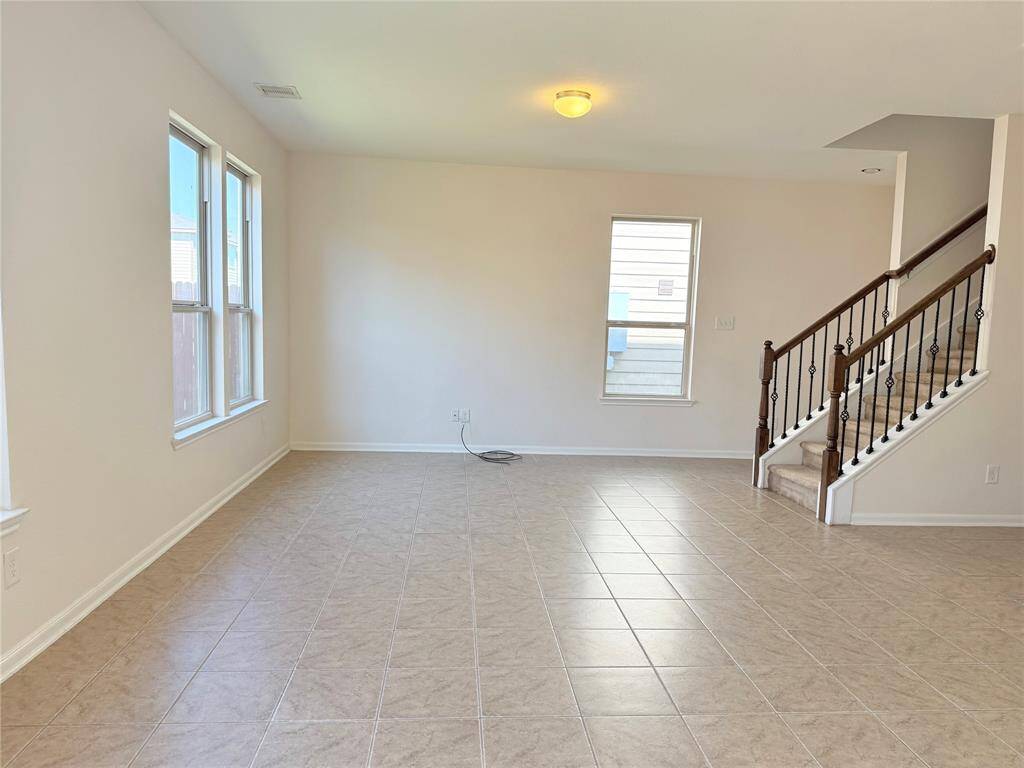 Bright, open living space with tiled floors, large windows for natural light, and a staircase with decorative railing leading upstairs. Ideal for a welcoming home environment.