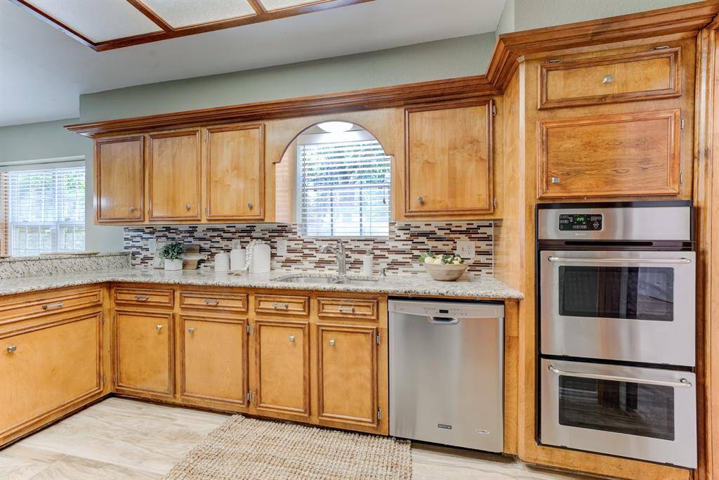 Enjoy cooking in a spacious and well-appointed kitchen with granite countertops, easy-to-clean stainless steel appliances, double ovens, ample natural light from the window over the sink, and a beautiful custom tiled backsplash.
