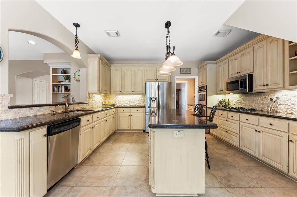 The kitchen features granite counterops, stone backsplash with undermounted lighting, a gas cooktop,  Double stainless steel ovens, and pendant lighting.