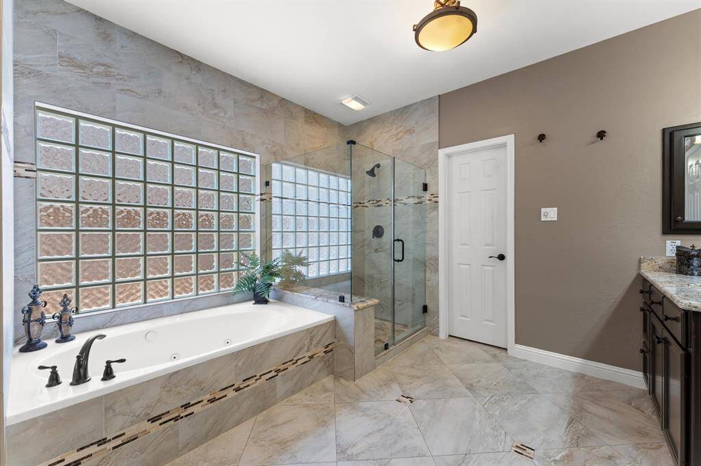 The primary bathromm has wall to ceiling tile, an oversized frameless glass shower, large whirlpool tub, decorative tile, and oil rubbed bronze fixtures.