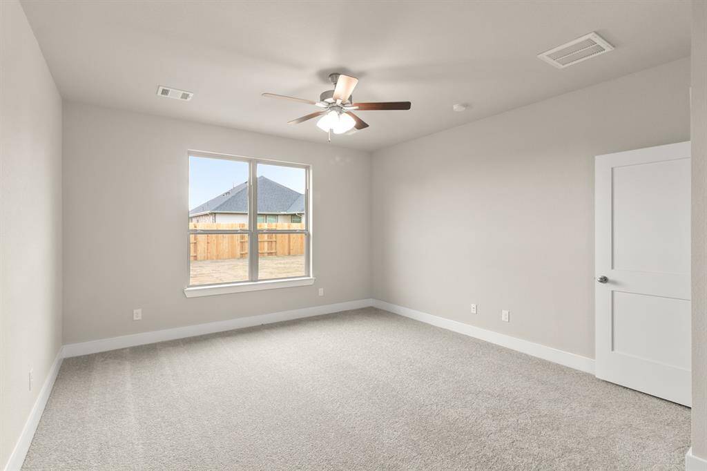 As you enter the primary bedroom, you’re greeted by an abundance of natural light pouring in through large, beautifully framed windows, casting a warm glow on the soft, neutral tones of the walls.