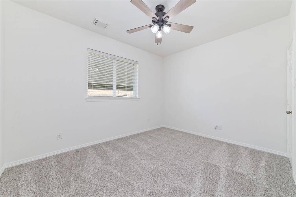 The first of the secondary bedrooms features new neutral carpet and walls, a ceiling fan with lights, and a window with blinds, offering a bright and versatile space.