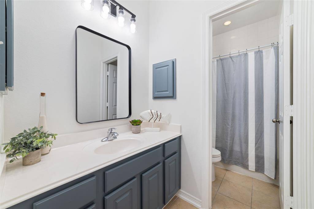 This full bathroom features a clean and modern design with a white countertop, updated lighting, dark cabinets, and a large mirror. It has a separate door for the shower and toilet area for functionality.  It is located in the hallway with the two secondary bedrooms but could also be used for guests.