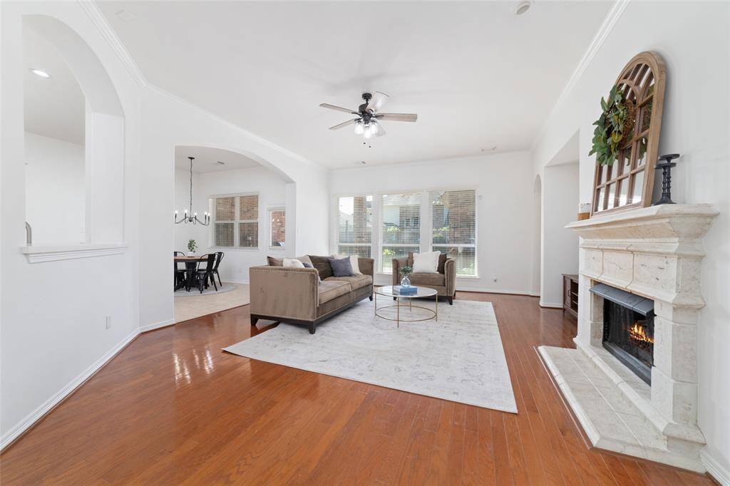 Bright and airy living room with hardwood floors, a cozy gas fireplace, and large windows. It opens to a kitchen area through an elegant archway, creating a spacious and inviting atmosphere.
