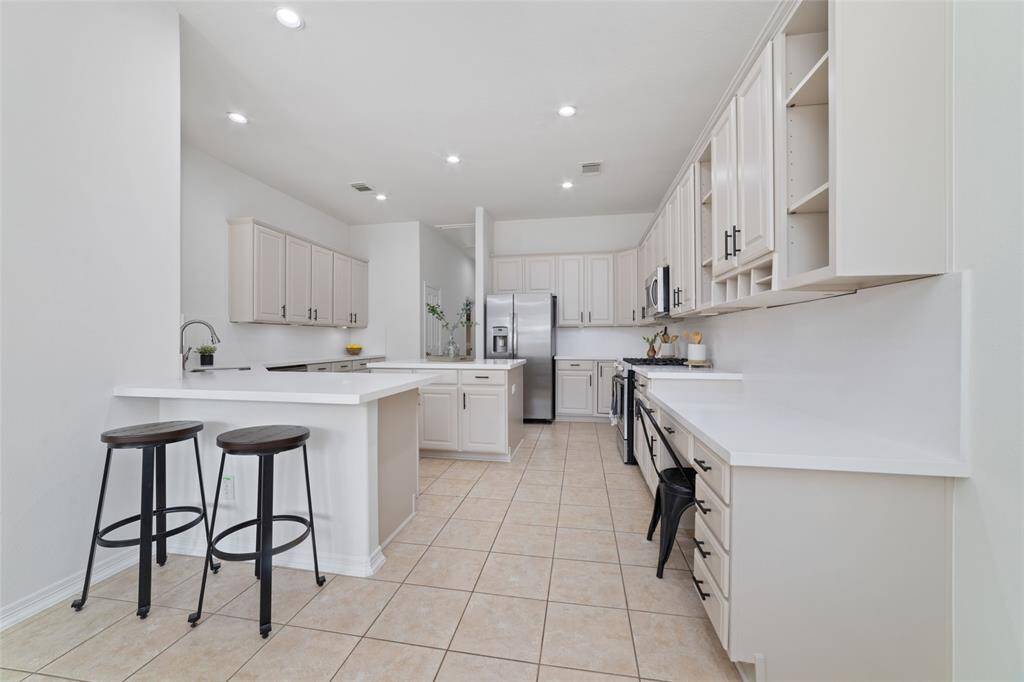 This updated kitchen features sleek freshly painted cabinetry, new Quartz countertops and backsplash, stainless steel appliances, black cabinet pulls, farmhouse sink and ample counter space. The open layout includes a breakfast bar with seating, perfect for casual dining. Recessed lighting and tile flooring complete the bright, inviting space.