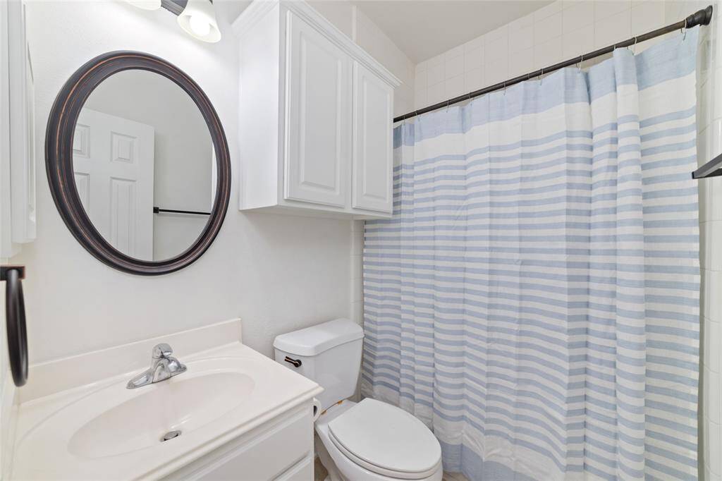 This second full bathroom features a clean, white design with a circular mirror above a simple vanity. Located just off the breakfast room and beside the third secondary bedroom.