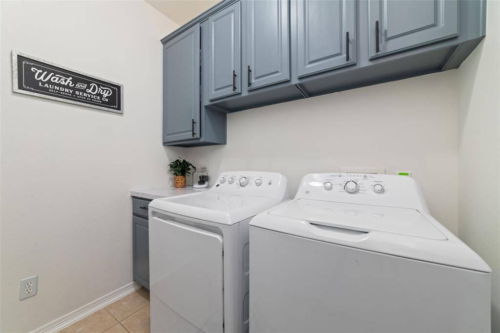 A large walk in laundry room with cabinets for storage and countertop space for folding laundry.  There is also extra fridge space.