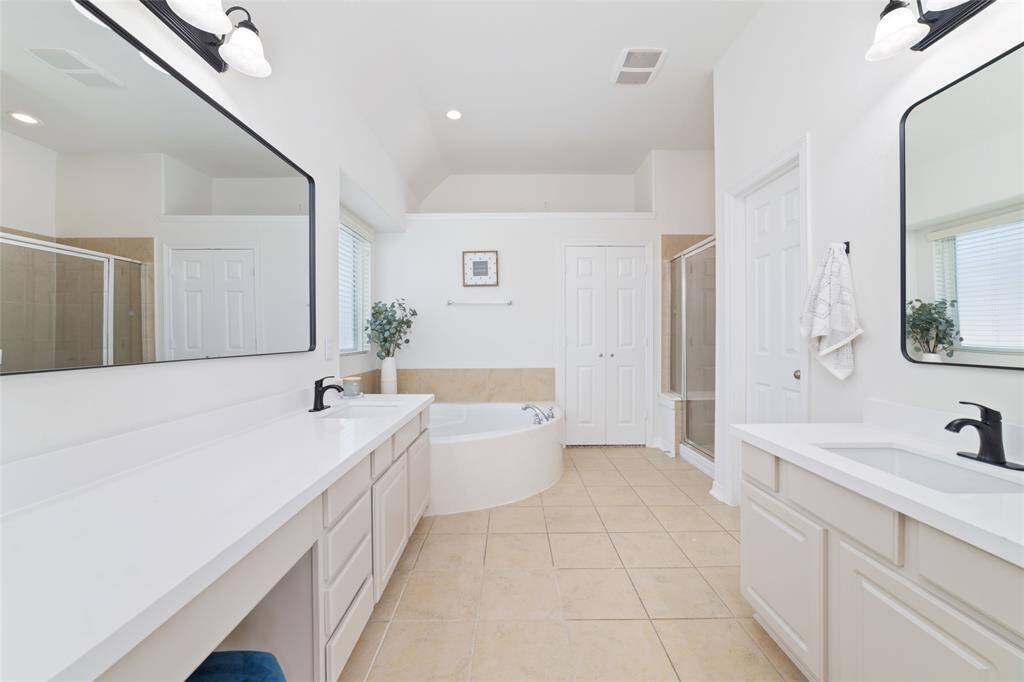 The spacious primary bathroom features dual sinks with modern fixtures, a large soaking tub, a separate shower, and ample storage. New Quartz countertops, updated mirrors, and lighting finish out the space.