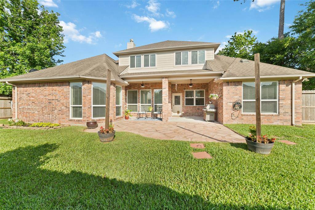 A spacious backyard with a well-maintained lawn, a brick exterior, and a cozy patio area perfect for outdoor gatherings. Large windows allow plenty of natural light, and the mature trees offer added privacy and shade. There is also a great side yard.