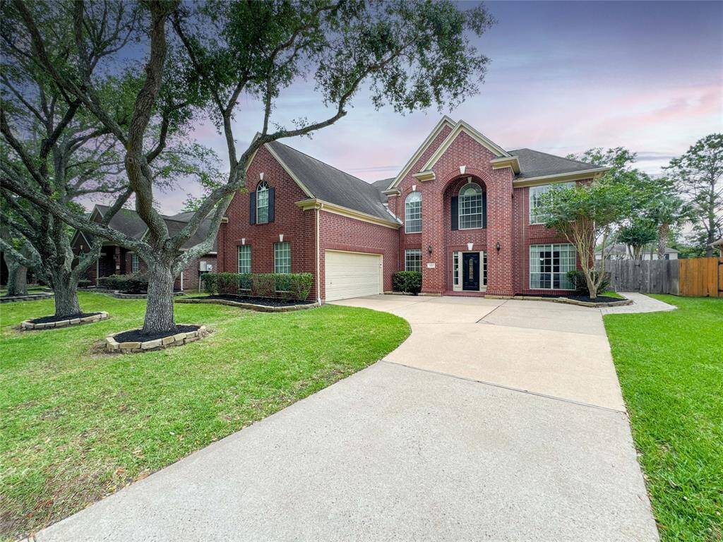 Welcome home to this classic two-story red brick home with large windows and a grand entrance. It has a spacious driveway leading to a two-car garage, surrounded by well-maintained landscaping and mature trees.