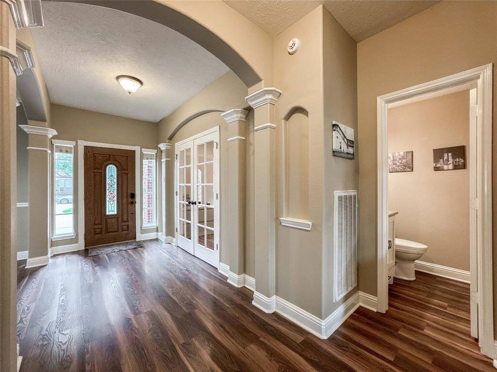 This photo showcases an elegant entryway with rich wood flooring, decorative arches, and French doors leading to the home office. It features a warmly lit space with a traditional wooden front door and a convenient half bathroom.