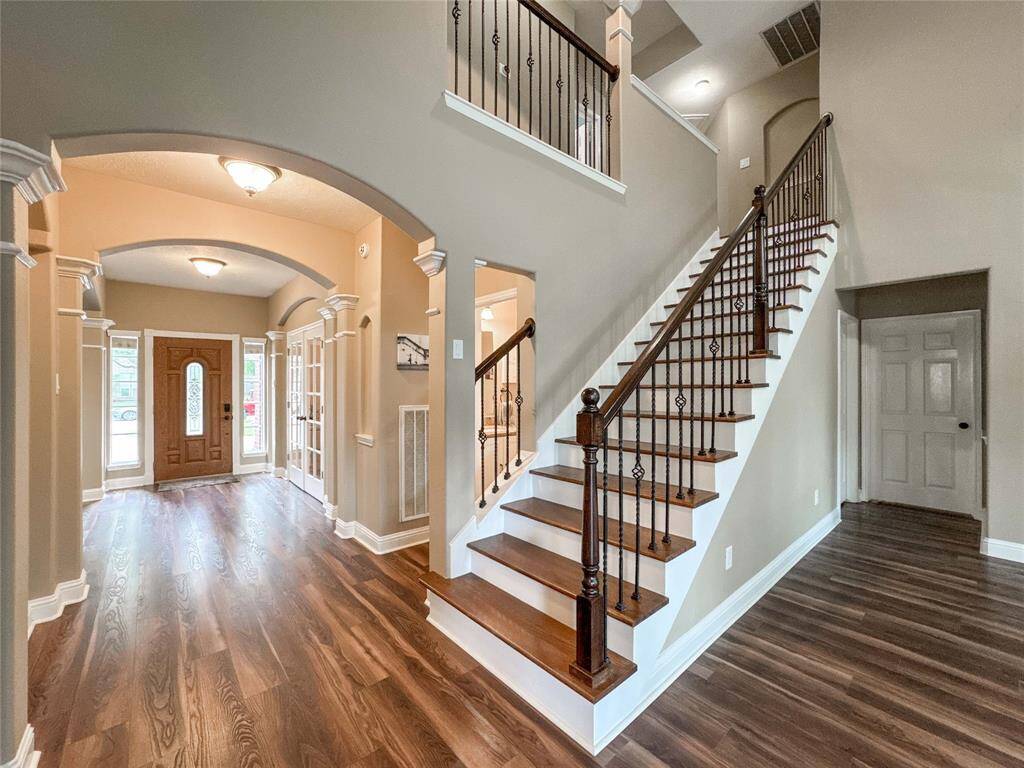 This inviting view features a the entryway and the grand staircase with dark wood accents adds a touch of sophistication, leading to an upper level that promises additional living space.