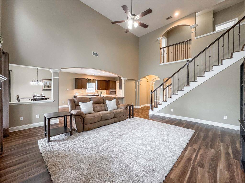This spacious living room features high ceilings, wood flooring, and an elegant staircase. An open layout connects to the kitchen and dining area, creating a welcoming atmosphere.