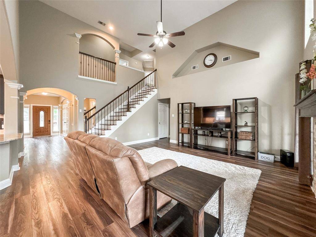 Spacious living room with high ceilings and elegant archways. Features a large staircase, wood flooring, and ample natural light. The open layout includes a cozy seating area and a modern entertainment setup, perfect for relaxing or entertaining.