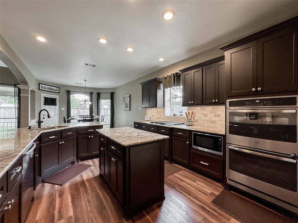 This spacious kitchen features elegant dark wood cabinetry, granite countertops, and modern stainless steel appliances. It includes a central island for additional prep space and a cozy breakfast area with large windows for natural light, offering a view of the backyard.