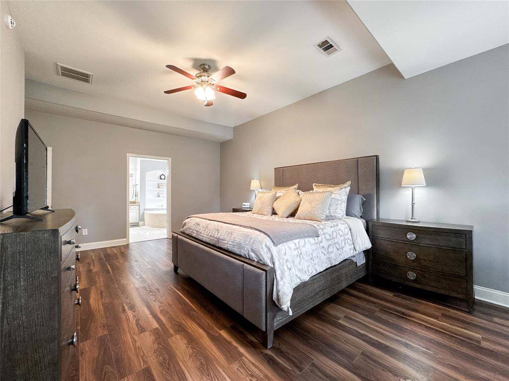 Spacious primary bedroom with elegant luxury vinyl floors, neutral gray walls, and a ceiling fan.