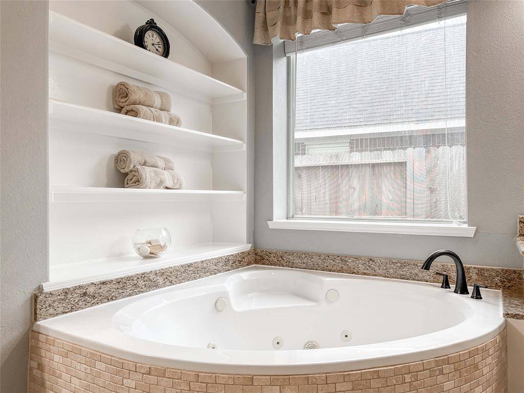 This bathroom features a spacious whirlpool tub with elegant tile surround, built-in shelving for storage, and a large window for natural light.