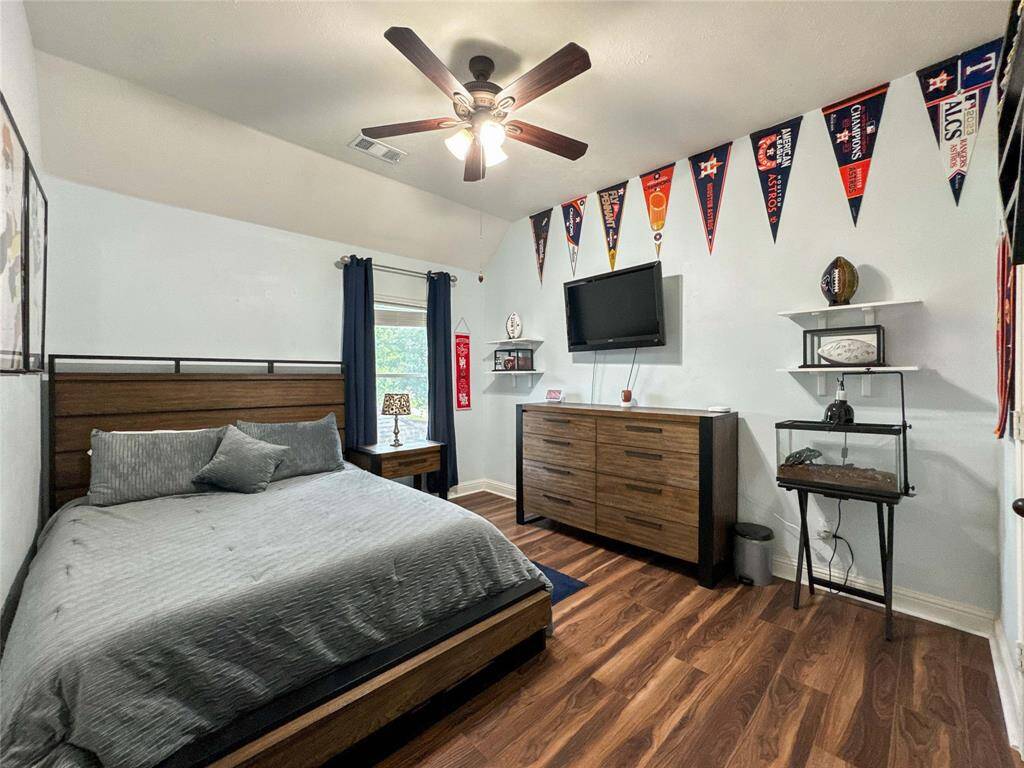 This secondary bedroom is found upstairs and features a cozy setup with a ceiling fan, and ample natural light from a window with dark curtains.