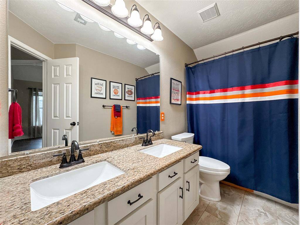 This upstairs bathroom features a double sink vanity with granite countertops, white cabinetry, and modern fixtures.