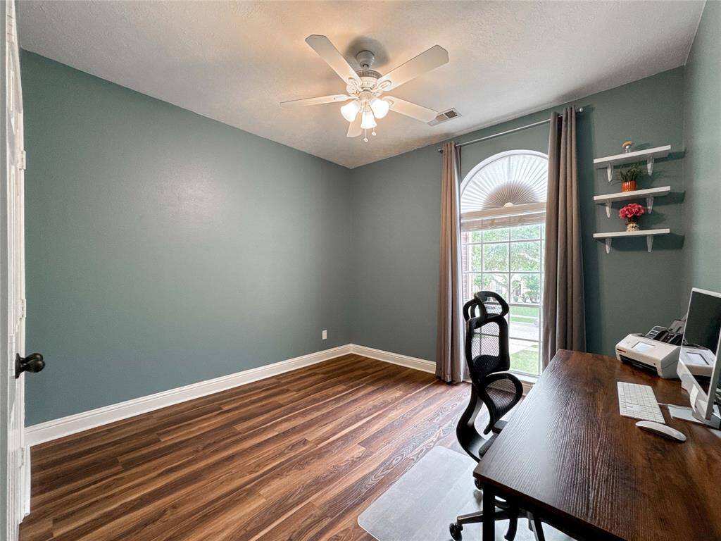 This photo shows a secondary bedroom upstairs with a large window providing natural light. It features a ceiling fan and hardwood floors. The walls are painted in a calming green, and there are shelves for decor or storage.