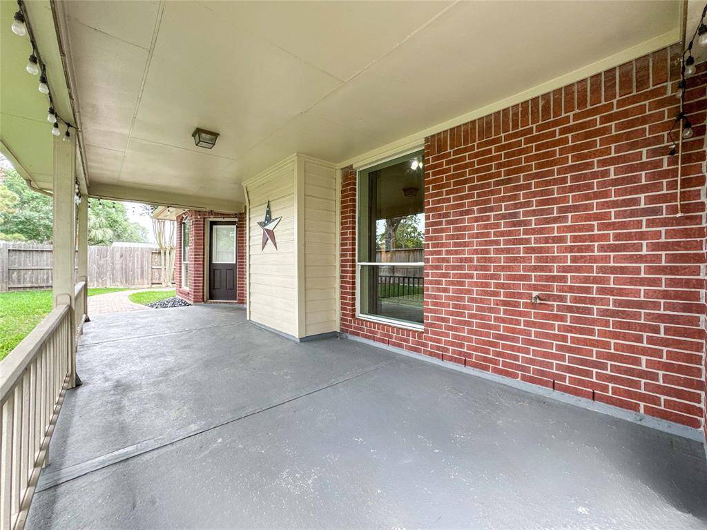 This covered  back patio space opens to a fenced backyard with a paved pathway, offering a cozy outdoor area for relaxation or entertaining.
