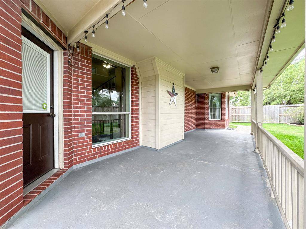This photo showcases a spacious covered patio with a red brick exterior. It features string lighting and overlooks a well-maintained lawn, perfect for outdoor relaxation and entertaining.