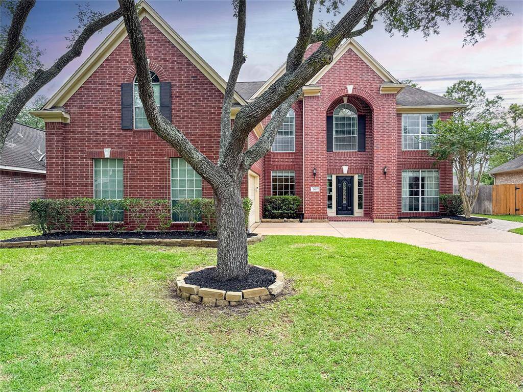 This elegant two-story red brick home features large windows, a welcoming double-door entrance, and a beautifully landscaped front yard with mature trees. Ideal for families seeking curb appeal and spacious living.