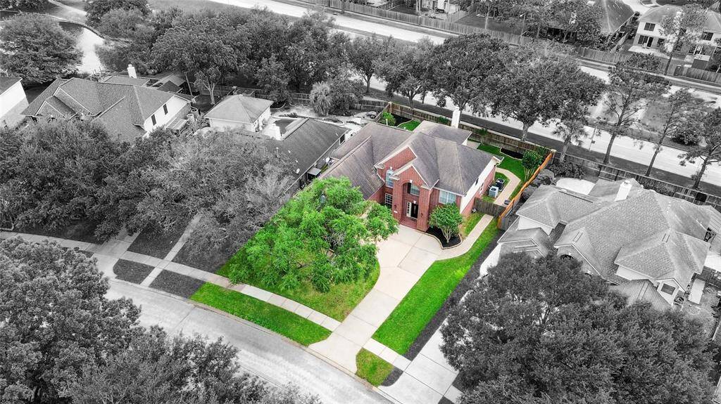This aerial photo showcases a beautiful red-brick home with a spacious driveway and well-maintained lawn. It's situated in a pleasant neighborhood with mature trees and nearby homes visible, offering a sense of community and privacy.