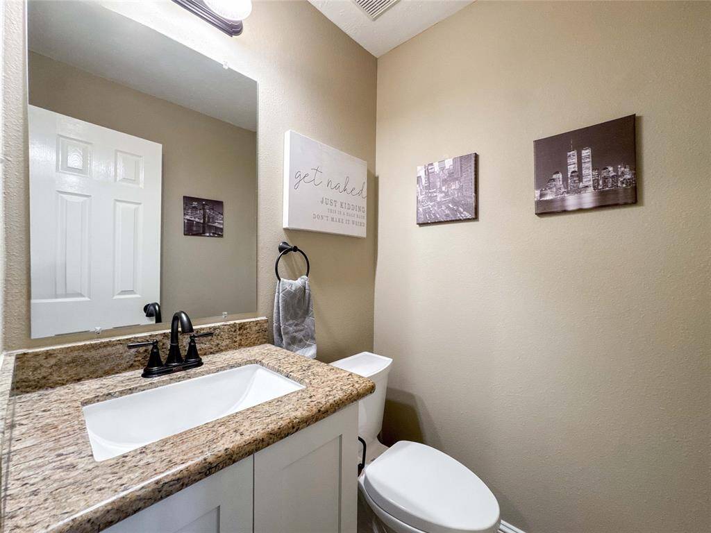 This is a cozy powder room featuring a granite countertop with a modern sink and black fixtures is located on the first floor before the stairs.
